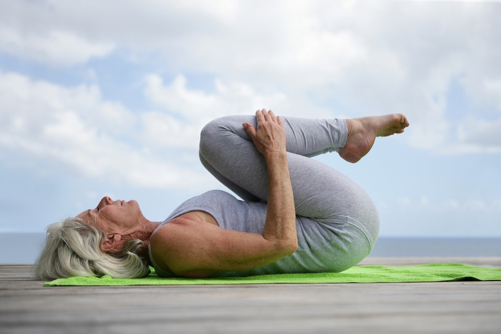 Old white woman doing laying and seated poses practicing several basic yoga poses