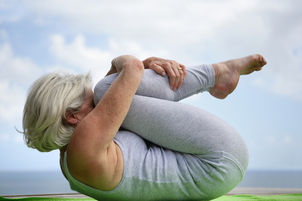 Lady over 50 years old doing a Hatha yoga pose on a green yoga mat 